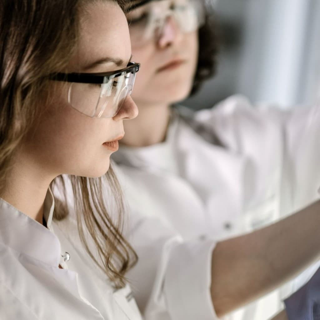 Two lab professionals wearing protective eyewear while conducting an experiment, focusing closely on their work for safety and accuracy.