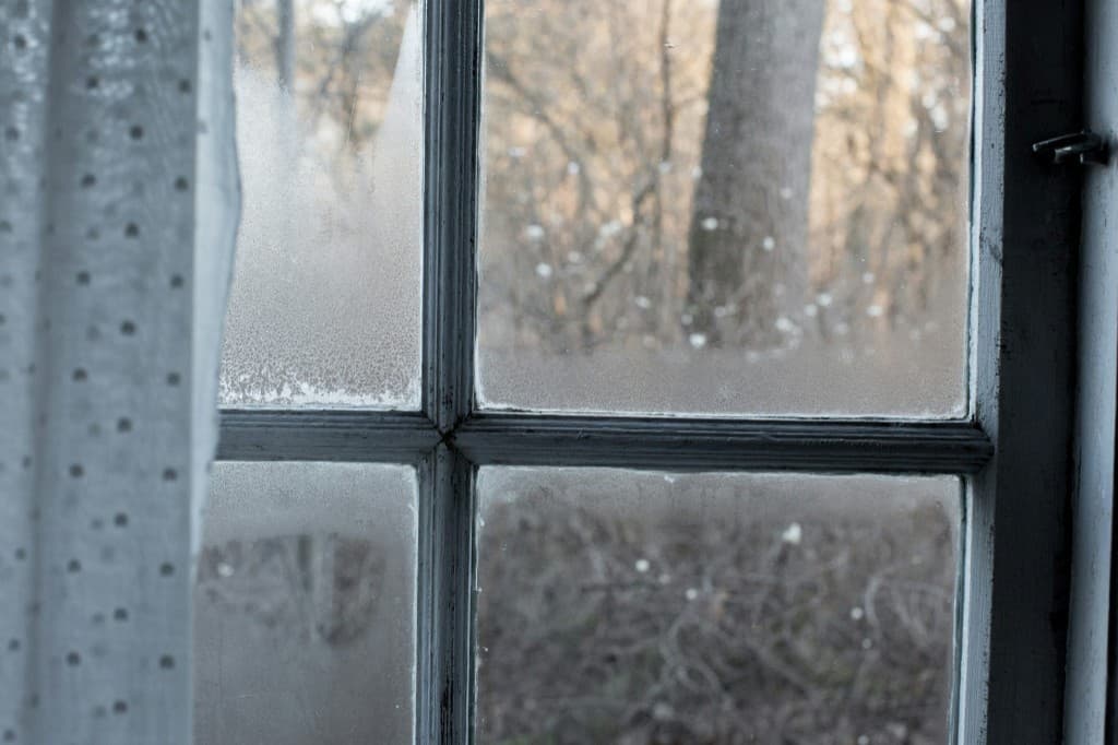 Window with condensation forming along cold glass panes, showing how moisture collects when warm indoor air meets a cool surface.