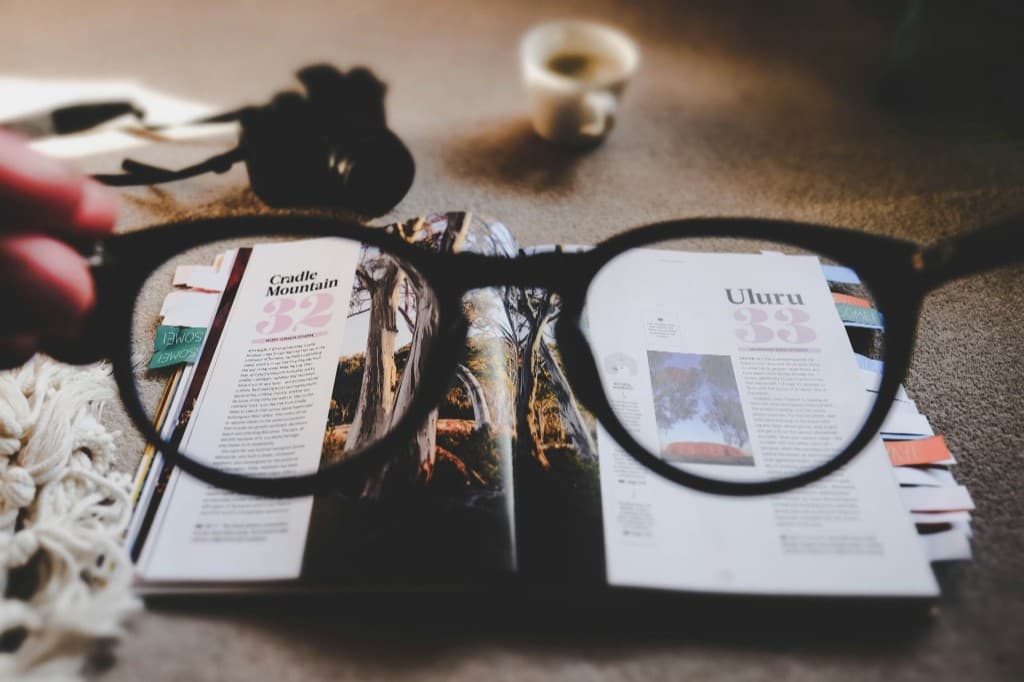 Glasses held in front of an open magazine, making the text appear sharper through the lenses to show the impact of clear vision.