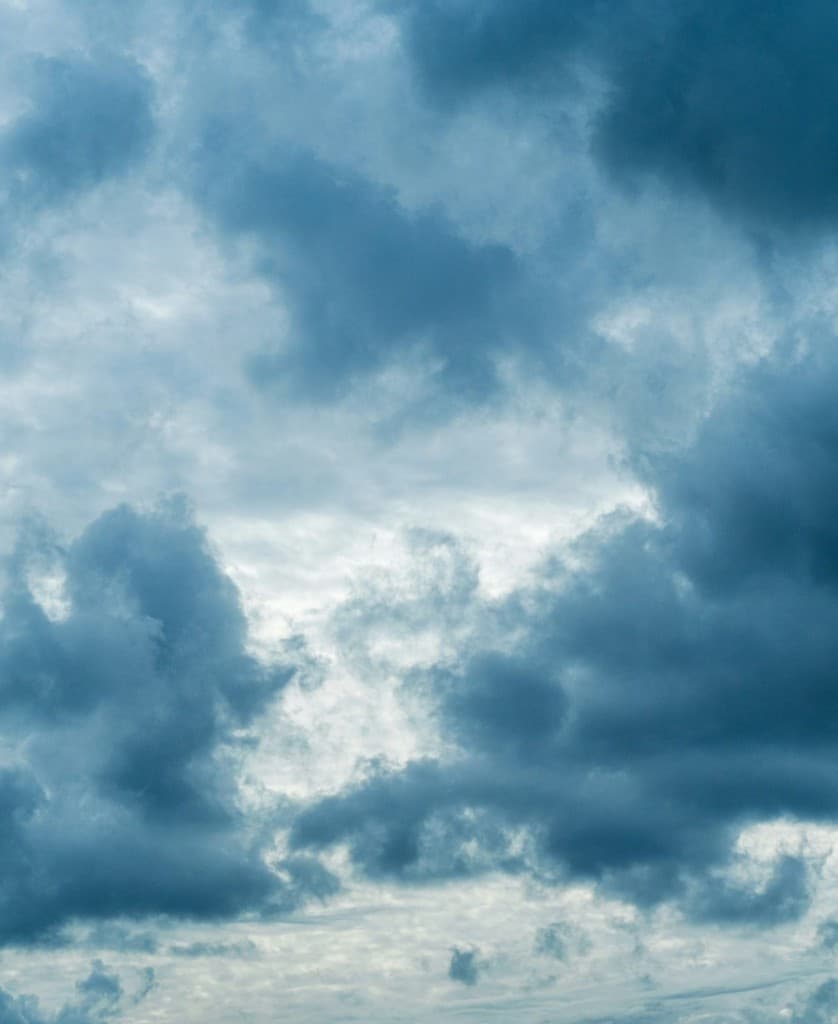 Overcast sky filled with thick gray and blue clouds, showing daylight filtering through cloud cover.