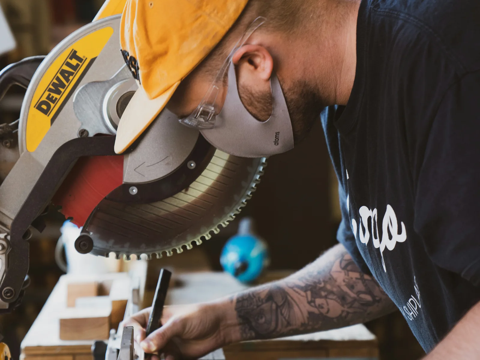 A carpenter in clear safety glasses and a dust mask marking a board at a mitre saw
